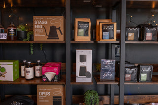 Shelves with coffee products including Fellow Stagg EKG Pro and Opus equipment, and Golden Lantern coffee bags.