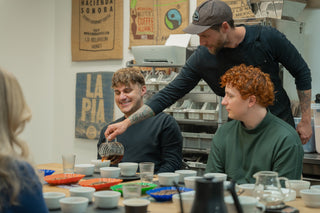 People sitting around a table with coffee mugs, engaging in a coffee tasting session.