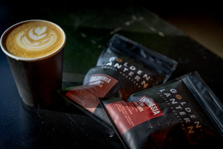 Cappuccino in a cup with Golden Lantern coffee packages on a dark surface