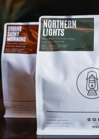 Two coffee bags labeled 'Bright Shiny Morning' and 'Northern Lights' on a wooden surface.